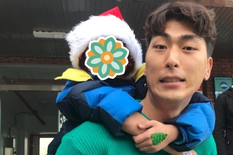 A volunteer carries a young child on his back. The child is wearing a Santa hat and their face is covered with a flower sticker, while the volunteer smiles at the camera.