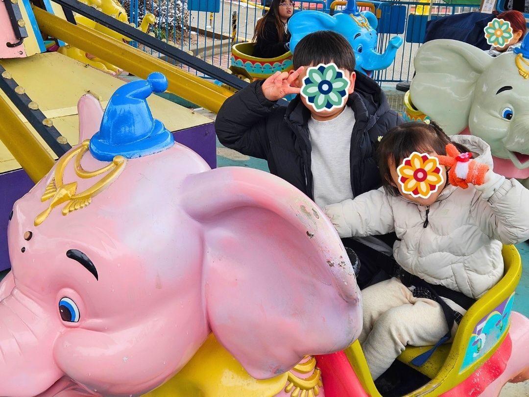Children riding an elephant-themed amusement park ride during a KKOOM trip.