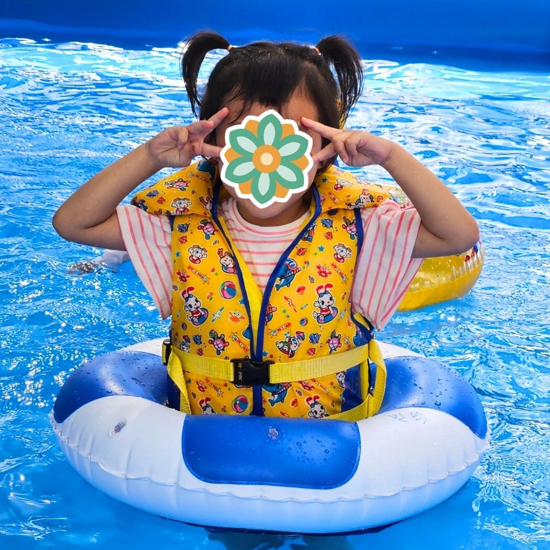 Child playing in a pool wearing a float ring during a KKOOM summer activity.