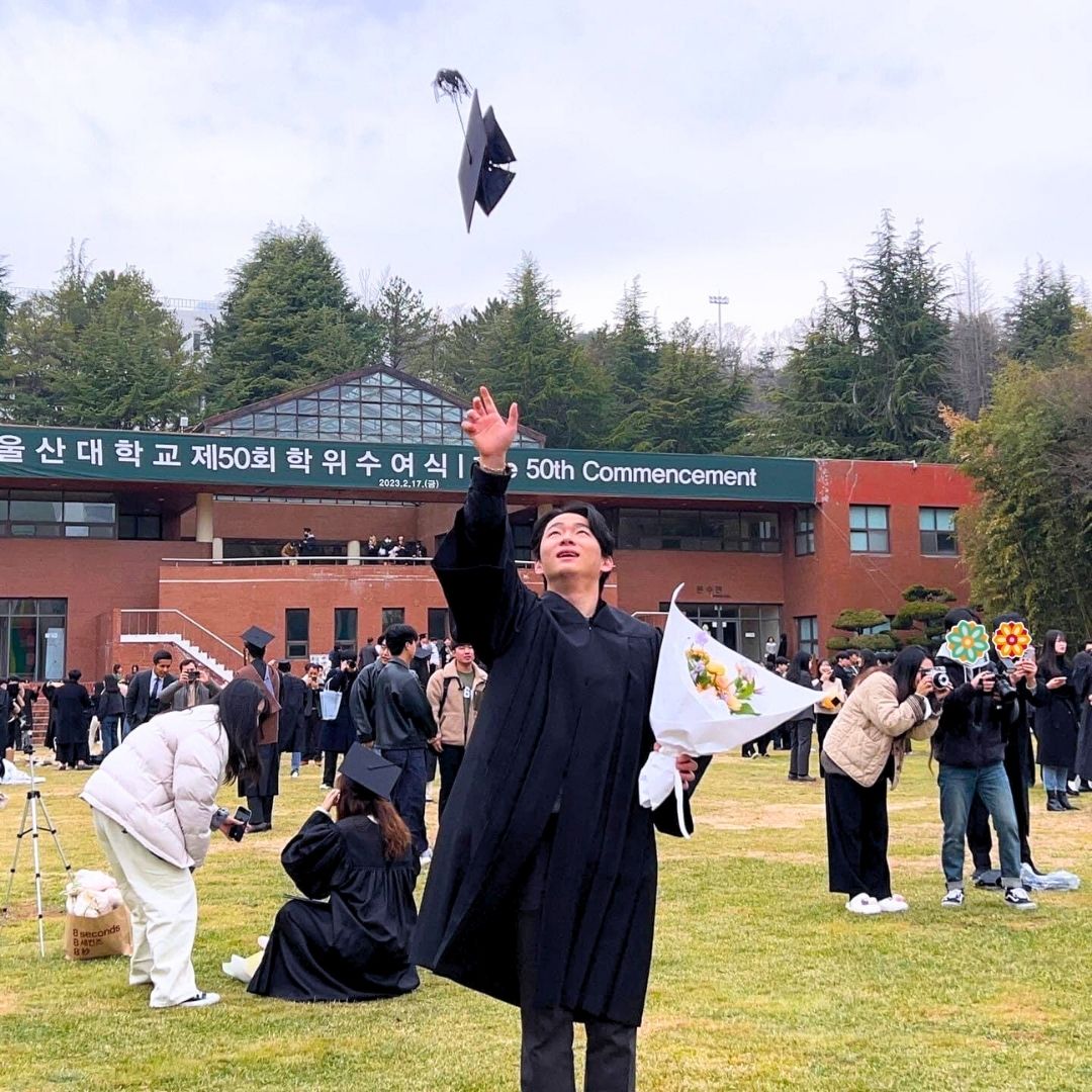 Student celebrating graduation outdoors while wearing a cap and gown.