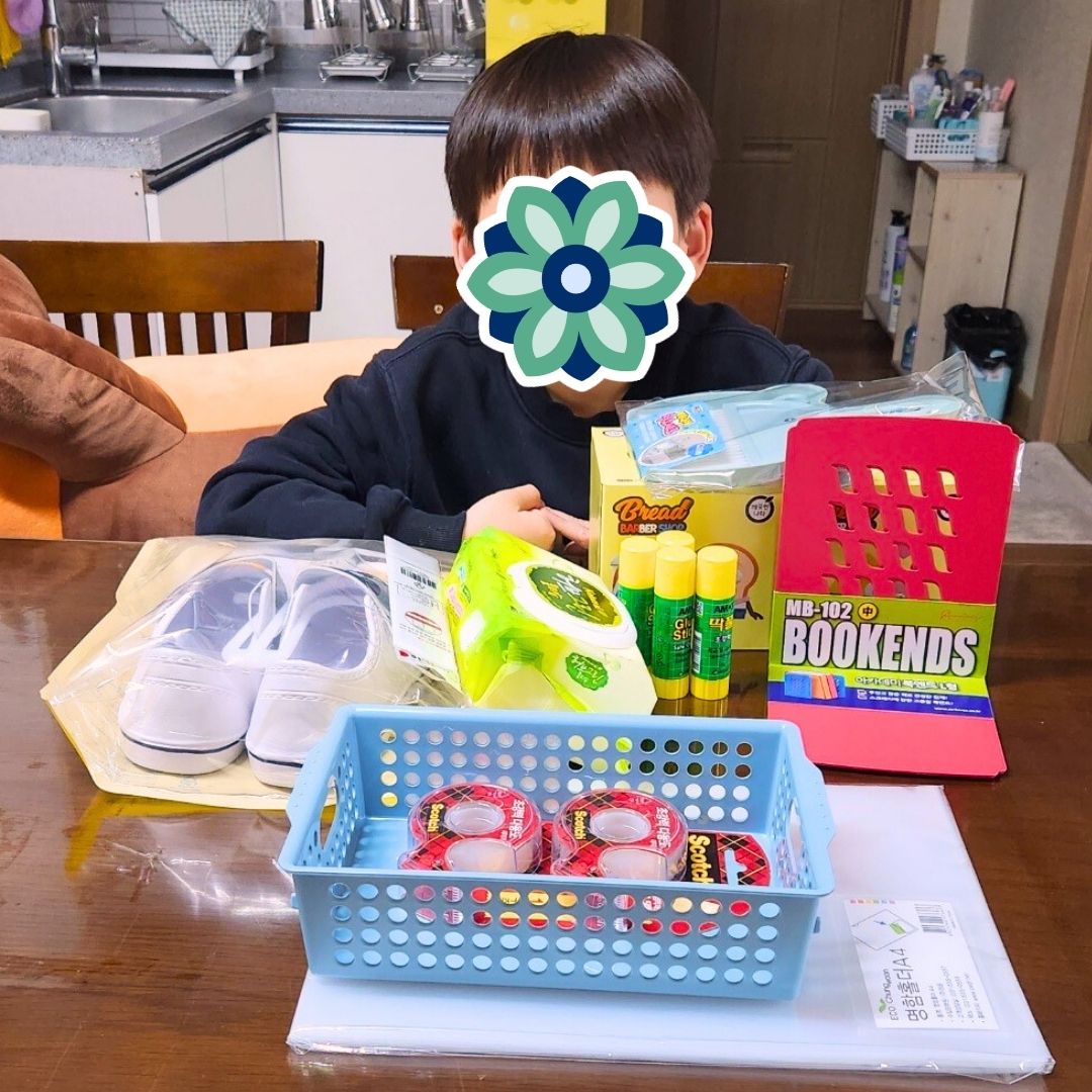 Child sitting at a table posing with school supplies donated from KKOOM.