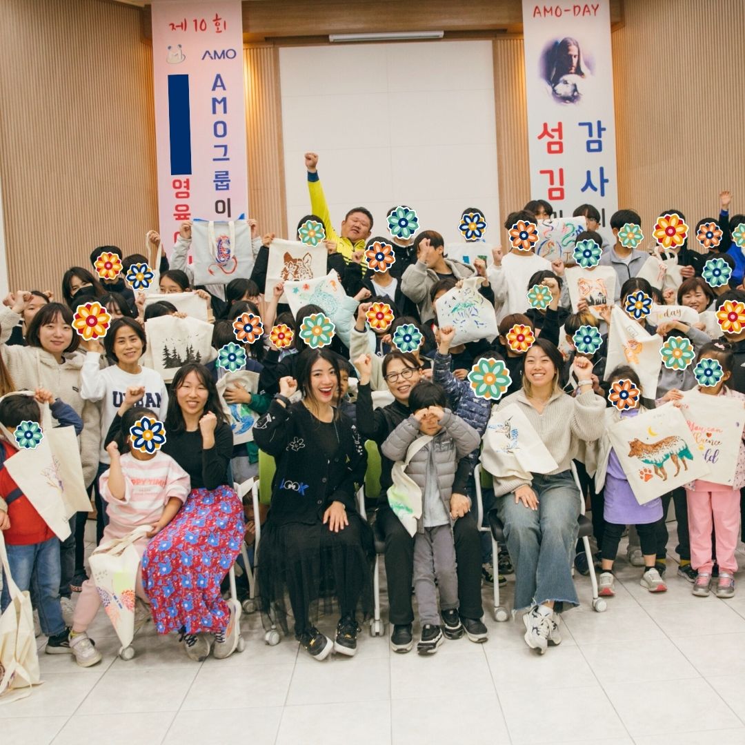 Large group of children and volunteers posing together during a KKOOM craft event.