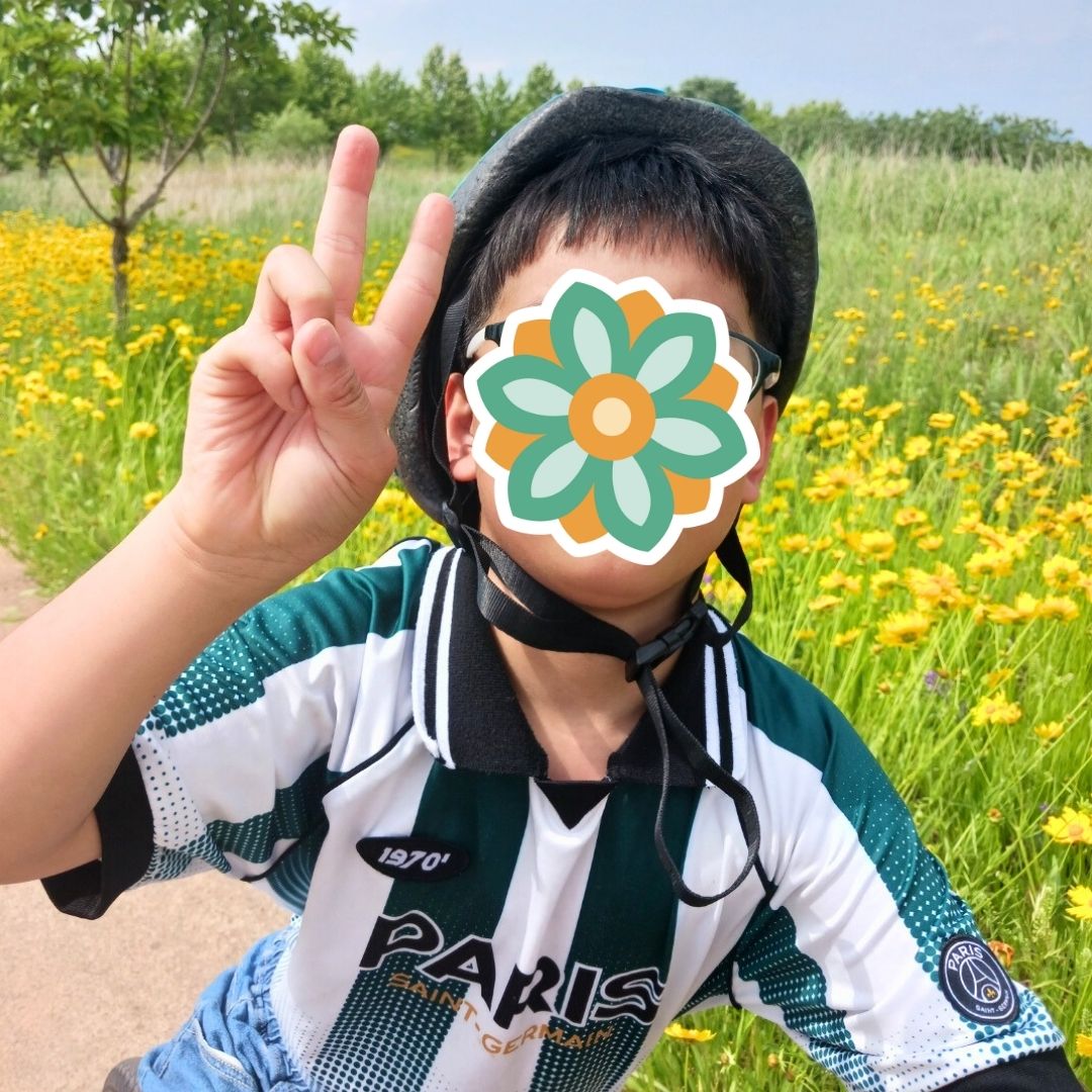 Child posing outdoors in a flower field while making a peace sign.