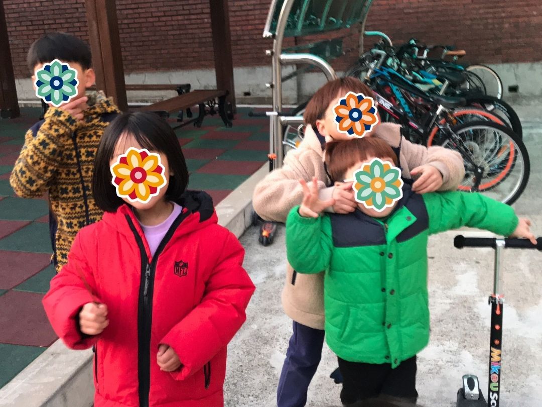 Children at a playground in Korea wearing winter jackets and smiling during a KKOOM visit.