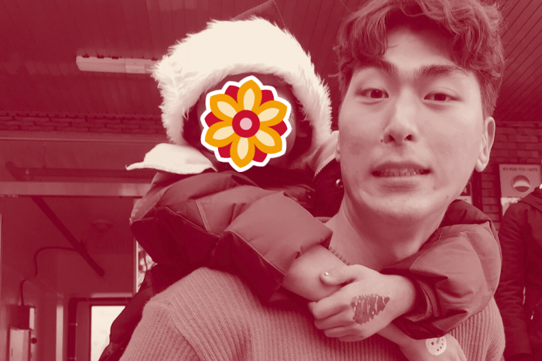 A man carrying a small child on his back indoors. The child’s face is covered with a flower sticker.