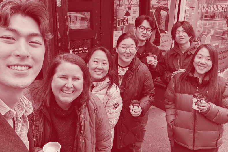 A group of people taking a close selfie outdoors, bundled in jackets, smiling closely together.