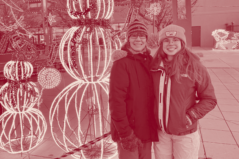 Jessie and her mom standing outdoors in winter coats next to large decorative light sculptures shaped like ornaments.