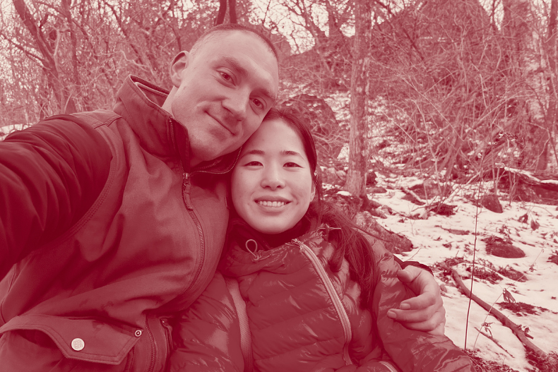 A couple taking a selfie outdoors in a snowy setting, bundled in winter jackets.