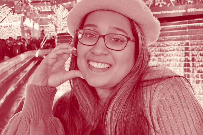 A woman wearing glasses and a light-colored hat smiling while seated indoors, possibly at a café or festive location.A woman wearing glasses and a light-colored hat smiling while seated indoors, possibly at a café or festive location.