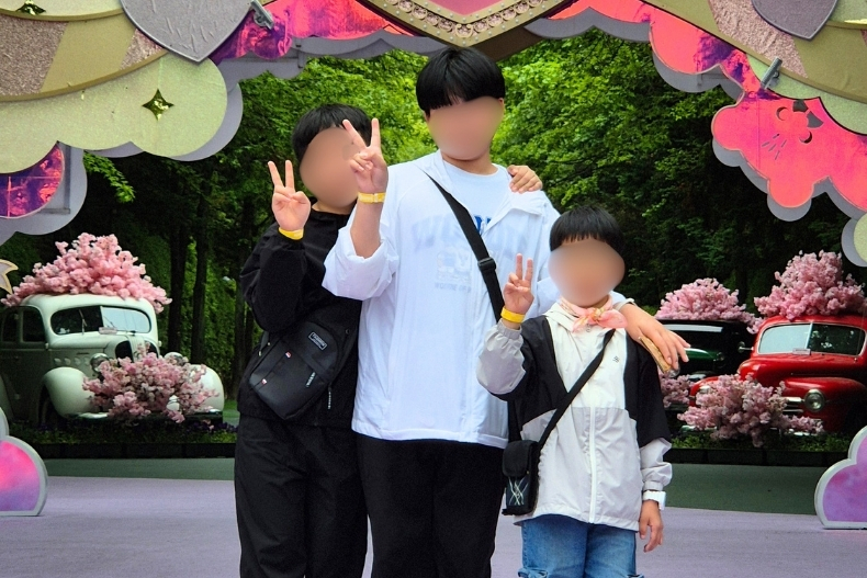Three boys posing together with peace signs in front of a colorful floral photo backdrop at an amusement park.