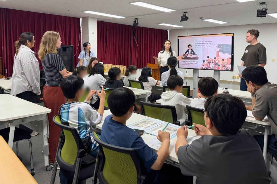 Students at a KKOOM workshop looking at a presentation screen, with volunteers and staff supporting the classroom.