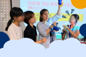 KKOOM volunteers and staff lead an interactive STEAM/English workshop activity with students, using visual aids and hands-on materials in a classroom setting.