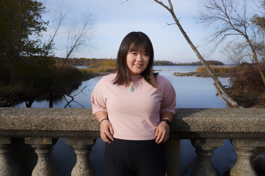 Vivian posing outdoors by a lake during the fall.